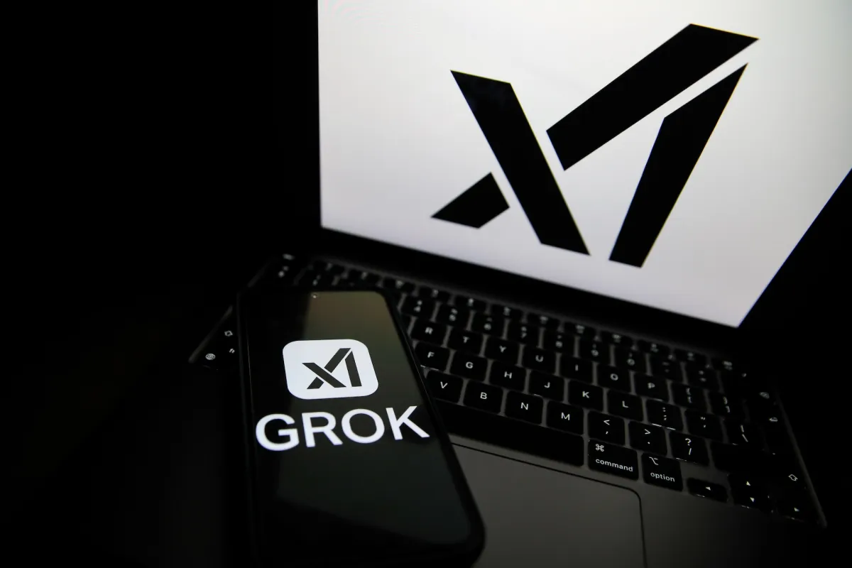 Smartphone displaying "GROK" and logo rests on a laptop keyboard, large logo on laptop screen.