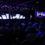 Large audience seated in a dimly lit conference hall watching a panel discussion on stage, with Ai4 2026 logos displayed.