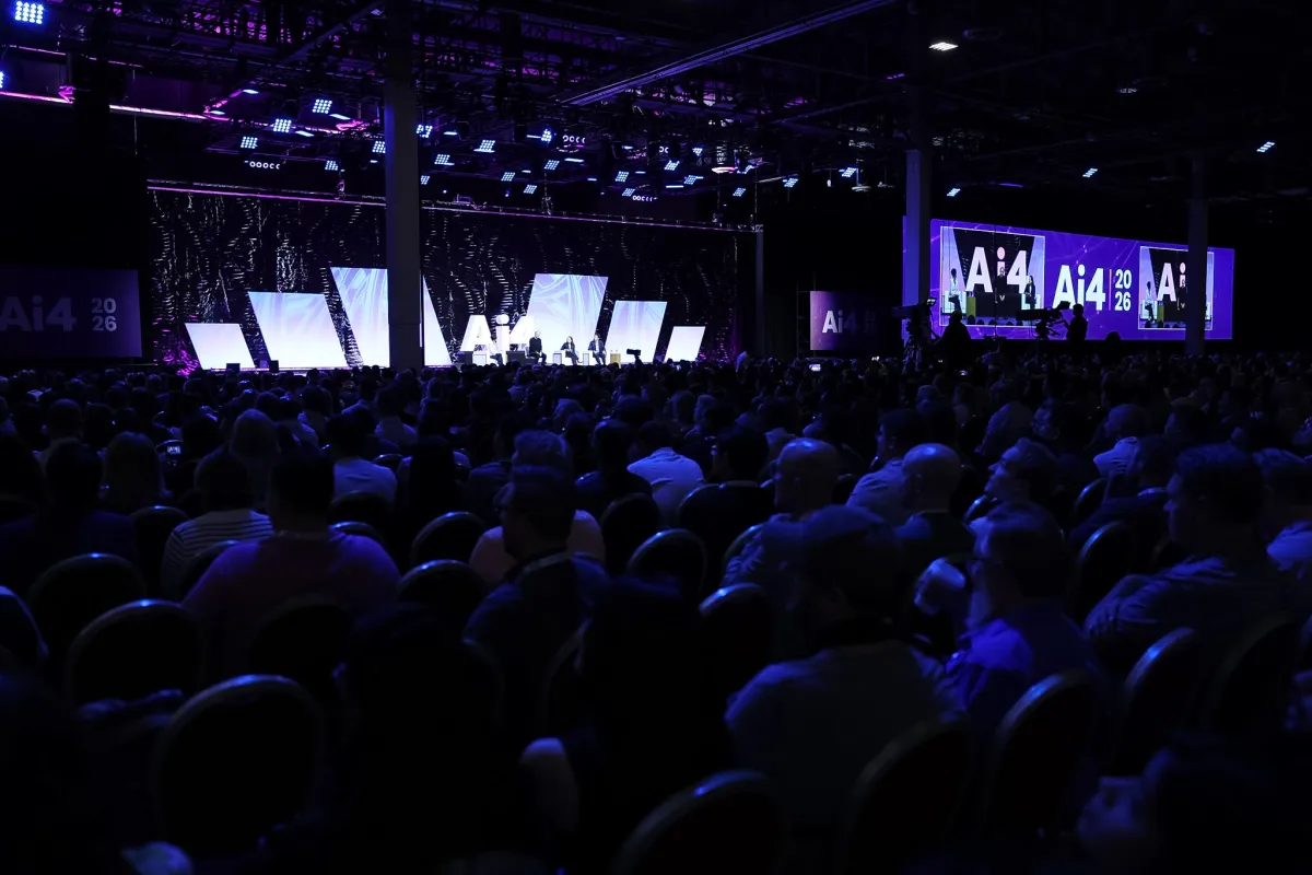 Large audience seated in a dimly lit conference hall watching a panel discussion on stage, with Ai4 2026 logos displayed.