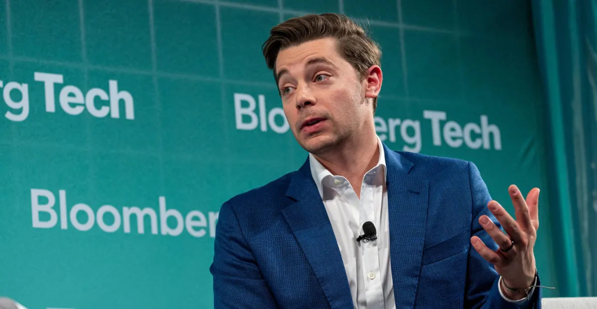 Person in blue suit speaking at Bloomberg Tech event, green backdrop with "Bloomberg Tech" text.