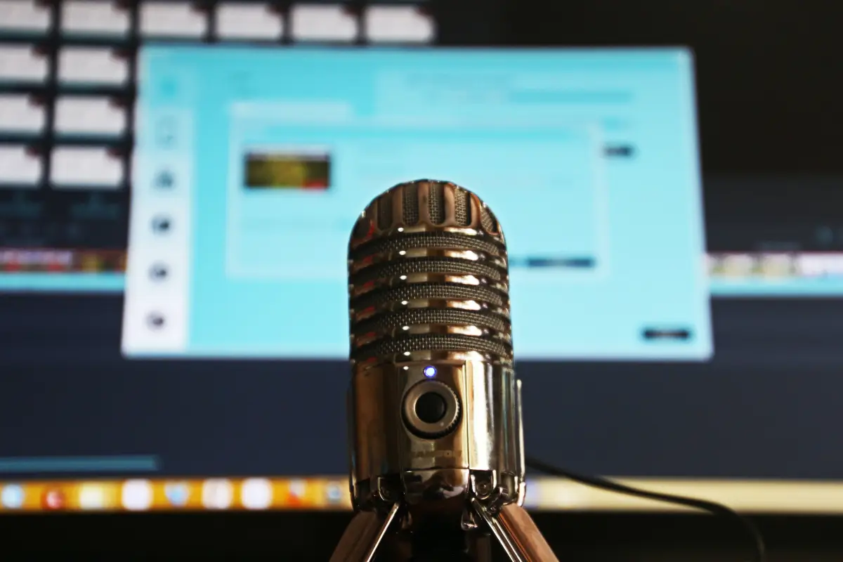 A silver microphone in focus with a blurred computer screen displaying a blue interface in the background.