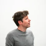 Man in a gray sweater looking to the side against a plain white background.