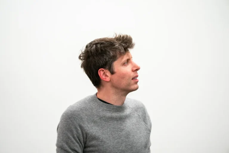 Man in a gray sweater looking to the side against a plain white background.