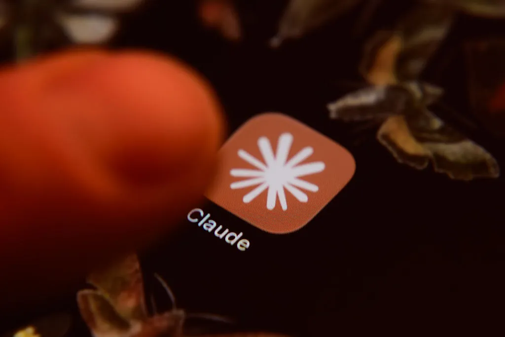 Finger touching a smartphone screen displaying an app icon labeled "Claude" with a starburst design.