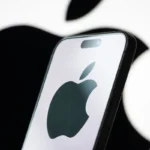 Smartphone displaying Apple logo in front of a larger Apple logo on a blurred background.