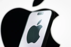 Smartphone displaying Apple logo in front of a larger Apple logo on a blurred background.