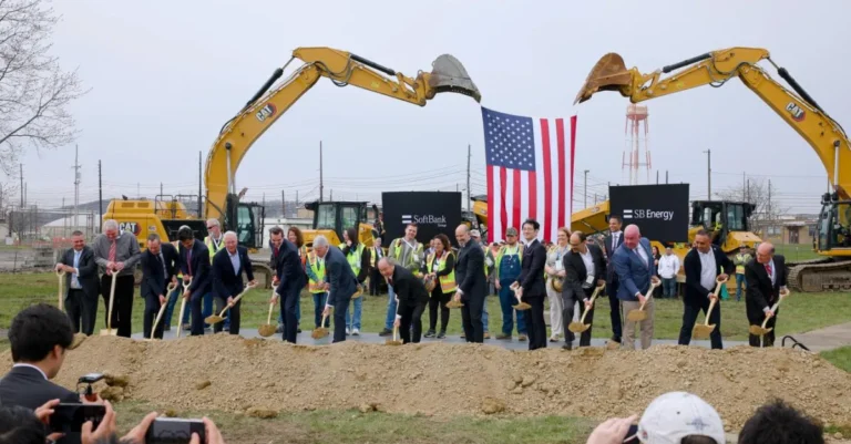 Group of people with shovels at a groundbreaking event, American flag and construction equipment in the background, SoftBa...