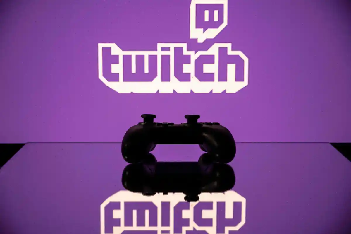 Game controller silhouette on reflective surface with large Twitch logo on purple background.