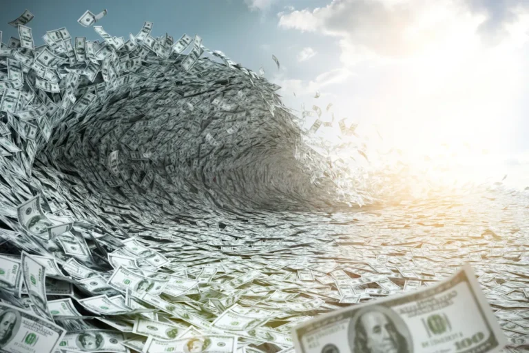 A wave of US hundred-dollar bills forming a tunnel under a partly cloudy sky.