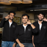 Three people in black jackets gesturing phone call in a modern office setting, with visible "Founding Team" text on their...