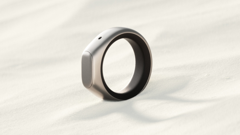 A sleek, modern ring with a metallic finish on a textured, light-colored surface, casting a soft shadow.