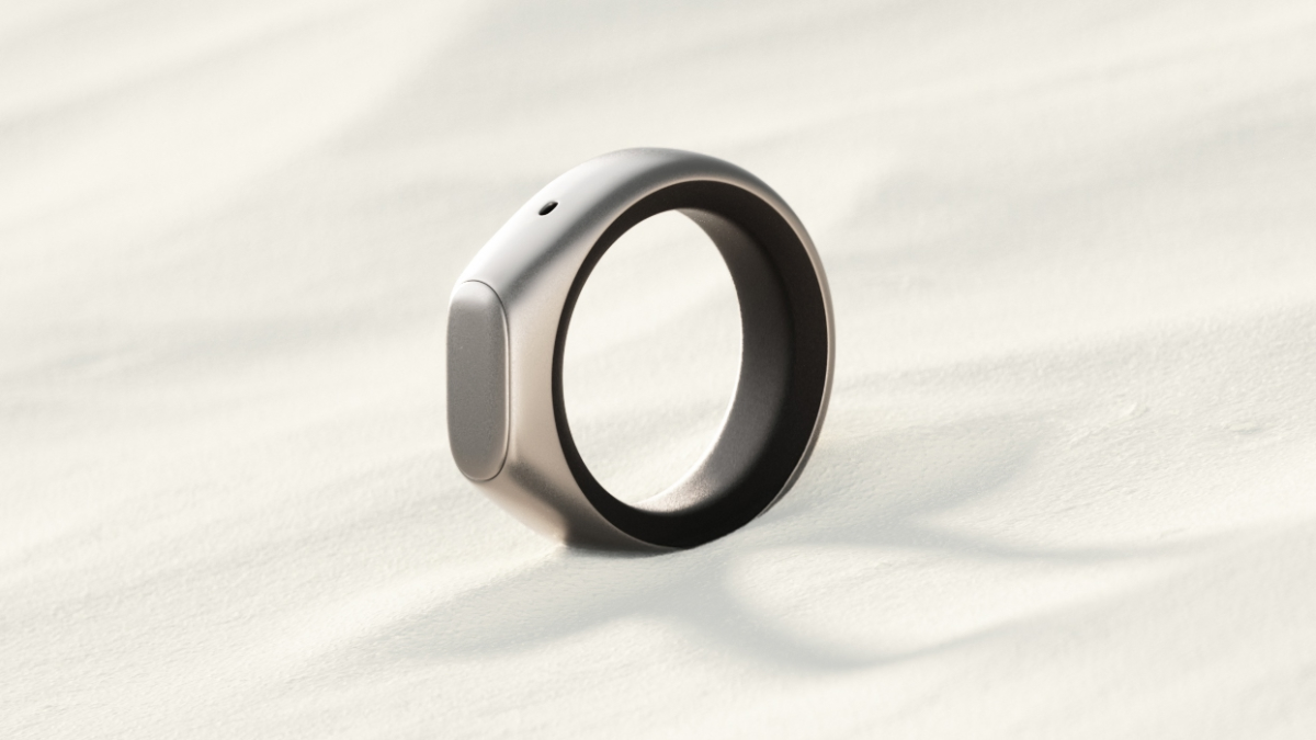 A sleek, modern ring with a metallic finish on a textured, light-colored surface, casting a soft shadow.