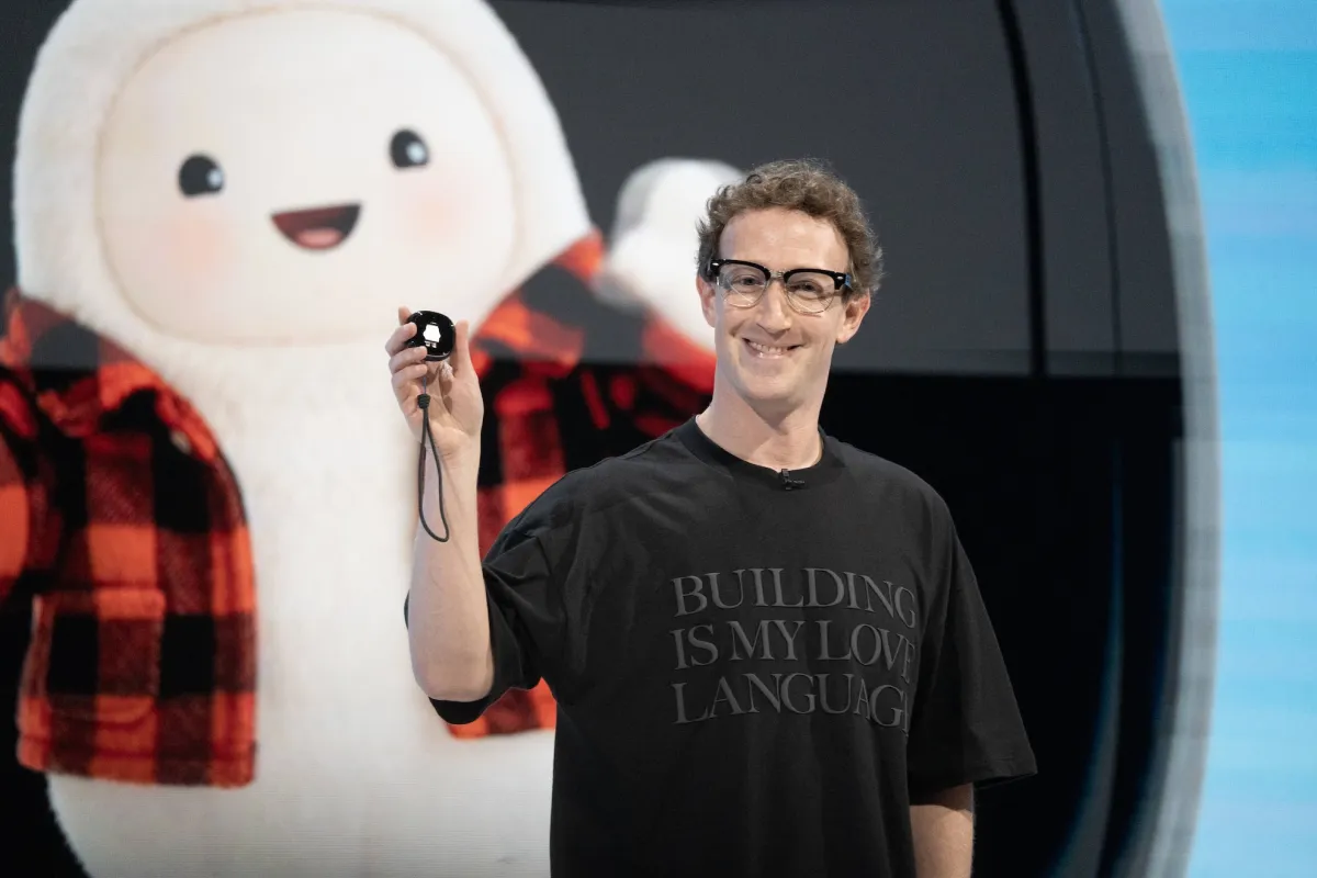 Man holding a small device, wearing glasses and a t-shirt with "BUILDING IS MY LOVE LANGUAGE" text, cartoon figure in back...