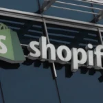 Shopify logo on a building facade, featuring a green shopping bag icon and white lettering against a glass background.