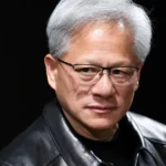 Person wearing glasses and a black leather jacket against a dark background.