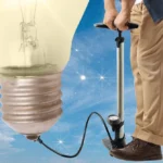 Man in khakis uses a foot pump connected to a giant light bulb, with a starry sky background.
