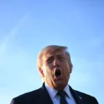 A man in a suit speaks passionately against a clear blue sky.