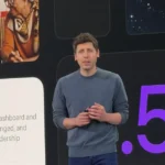 Man in a gray sweater speaks on stage with slides showing elderly women using a smartphone and text about a weekly busines...