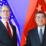 Two men in suits stand in front of U.S. and Chinese flags, posing for a photo.