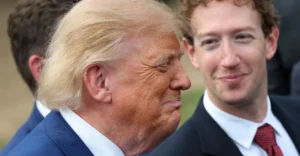 Two men in suits, one with blond hair smiling slightly, the other with curly hair looking at him, outdoors.