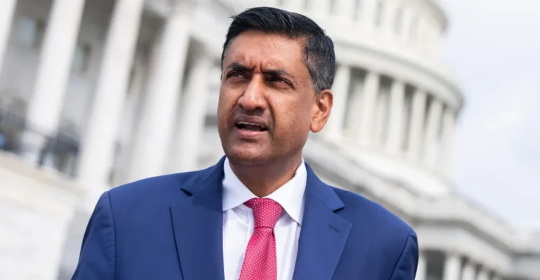 Man in a blue suit and red tie speaking outside a building with white columns in the background.
