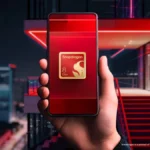 Hand holding a smartphone displaying Snapdragon 8 Elite Gen 3 logo, with a modern building and red neon lights in the back...