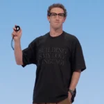 Person holding a small device on stage, wearing a black shirt with "BUILDING IS MY LOVE LANGUAGE" text, Meta logo in corner.