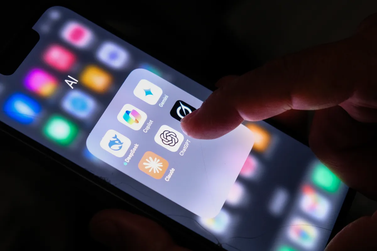 Finger tapping the ChatGPT app icon on a smartphone screen, surrounded by other AI app icons.