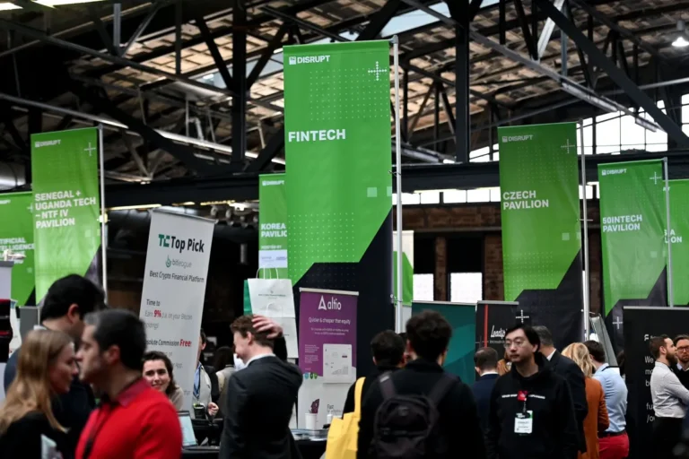 Crowded expo hall with green banners for fintech, Czech, and Korea pavilions, people conversing, and tech displays.