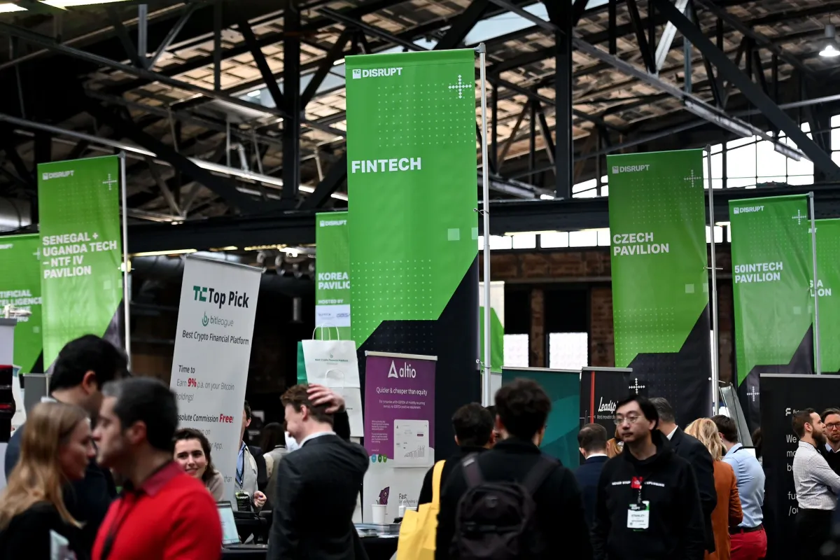 Crowded expo hall with green banners for fintech, Czech, and Korea pavilions, people conversing, and tech displays.