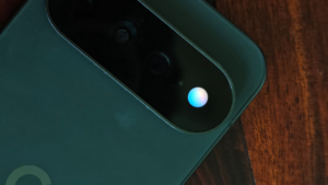 Close-up of a smartphone's camera module with a glowing blue and white light, placed on a wooden surface.