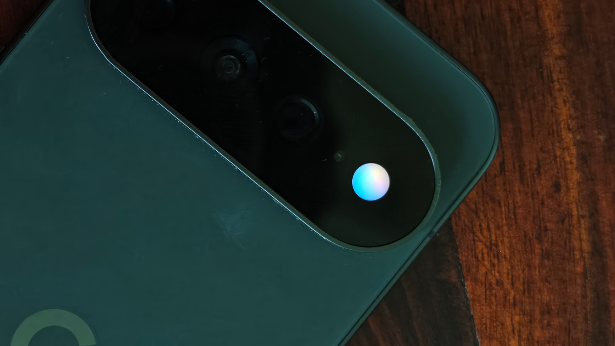 Close-up of a smartphone's camera module with a glowing blue and white light, placed on a wooden surface.