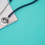Stethoscope resting on an open calendar against a turquoise background.