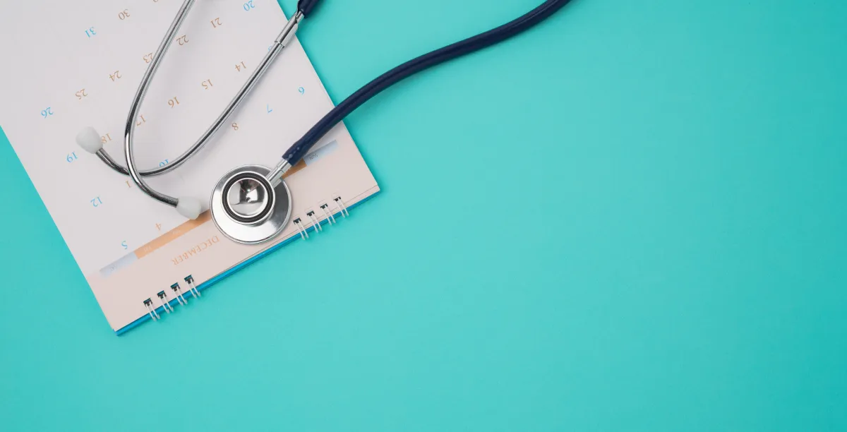 Stethoscope resting on an open calendar against a turquoise background.