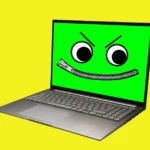 Laptop with a green screen displaying a cartoon face with large eyes and a zipper mouth on a yellow background.
