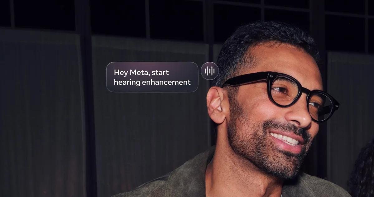 Man wearing smart glasses smiles, on-screen text reads "Hey Meta, start hearing enhancement.