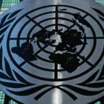 United Nations emblem on a building facade with grid-like windows in the background under a clear blue sky.