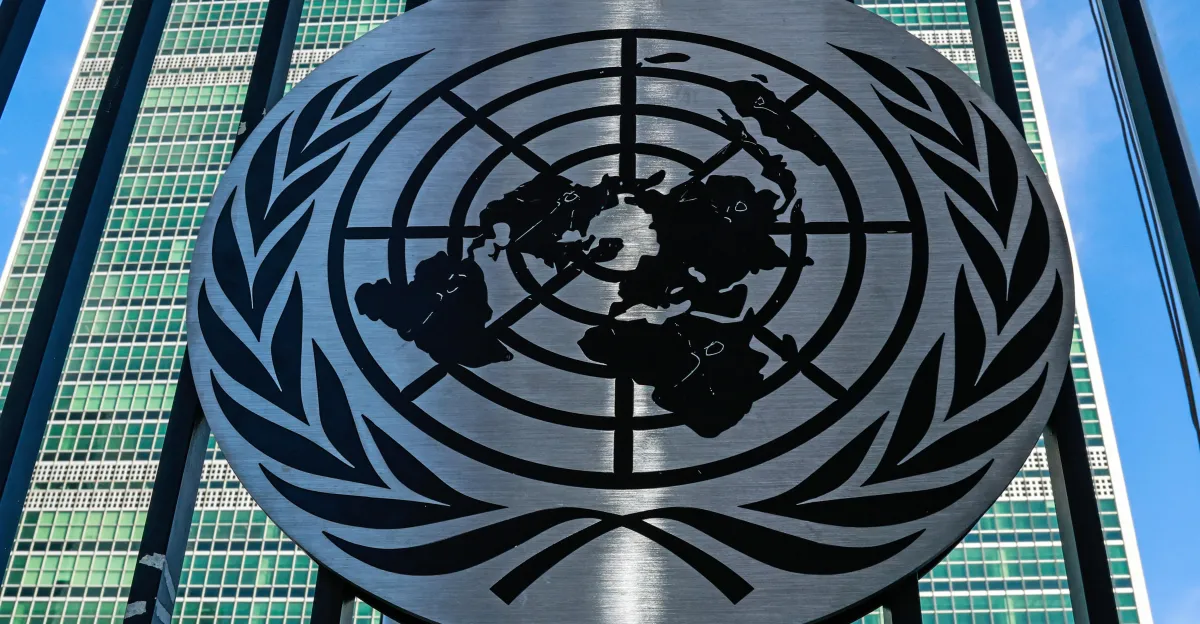 United Nations emblem on a building facade with grid-like windows in the background under a clear blue sky.