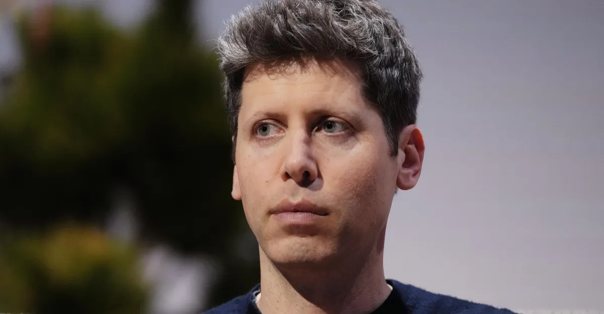 A person with short hair looks to the side against a blurred background, wearing a dark shirt.