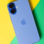 Blue iPhone with dual cameras on a yellow and green background.
