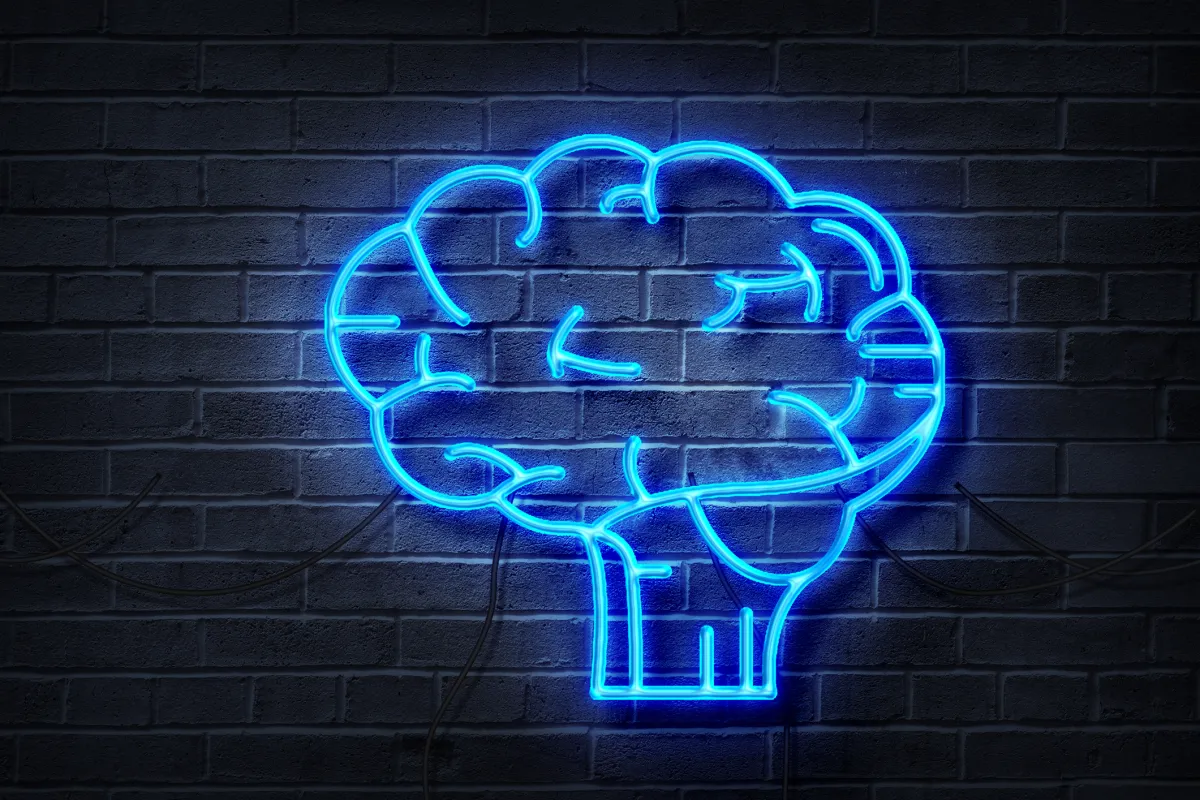 Blue neon brain sign on a dark brick wall background.