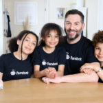 Four people wearing matching Fambot t-shirts sit at a table, smiling, with a plush toy nearby.