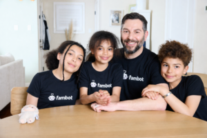 Four people wearing matching Fambot t-shirts sit at a table, smiling, with a plush toy nearby.