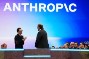 Two men on stage in discussion, one holding a microphone, with a smiling audience and "Anthropic" logo in the background.