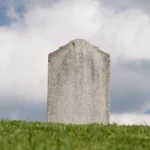 Gray tombstone on a grassy hill under a cloudy sky.