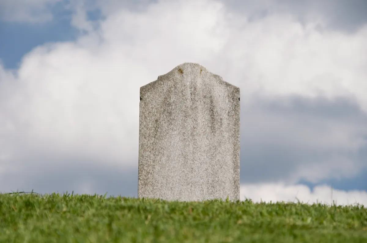 Gray tombstone on a grassy hill under a cloudy sky.