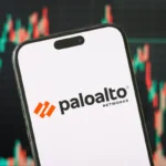 Smartphone displaying Palo Alto Networks logo, set against a blurred background of colorful stock market graphs.