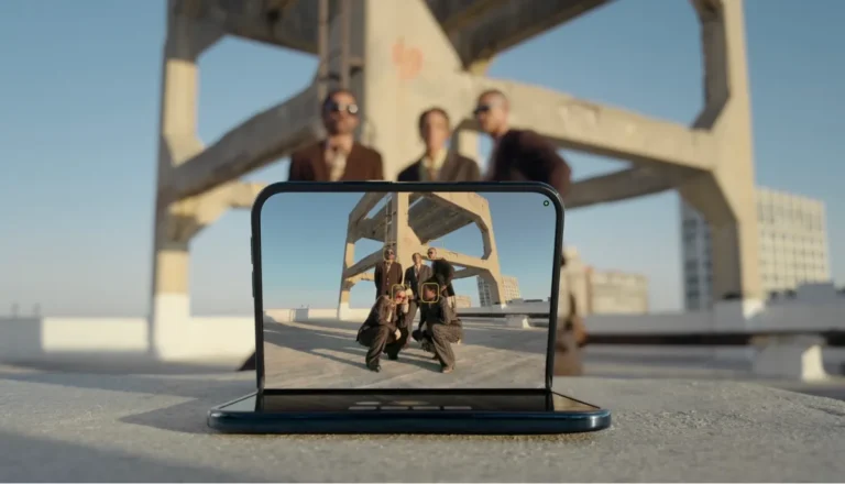 Foldable phone on a rooftop displaying a group photo with four people and an industrial structure in the background.