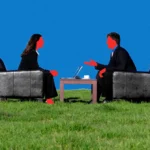 Two people in suits converse over a laptop on chairs in a grassy field, against a vivid blue background.