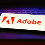 Smartphone displaying Adobe logo on a laptop keyboard, illuminated with purple light.